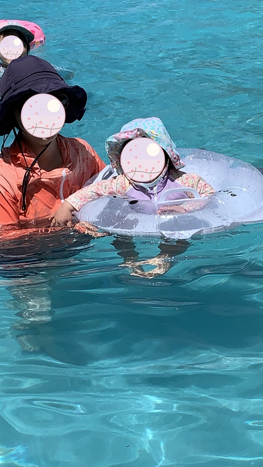 ハート柄の浮き輪で浮かぶ子どもと寄り添う親子