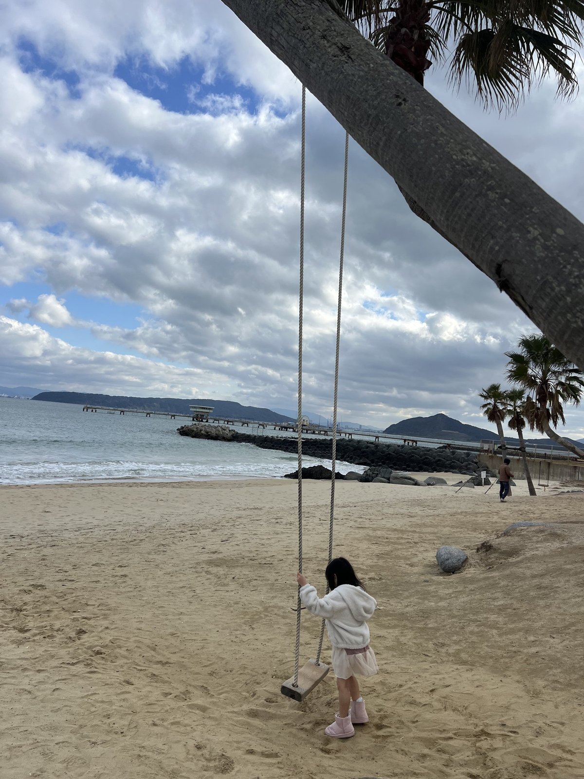ヤシの木ブランコに向かって砂浜を歩く娘