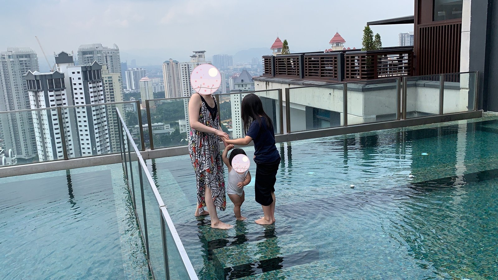 Walking along the edge of the rooftop pool with my child. The Kuala Lumpur skyline stretches out behind us